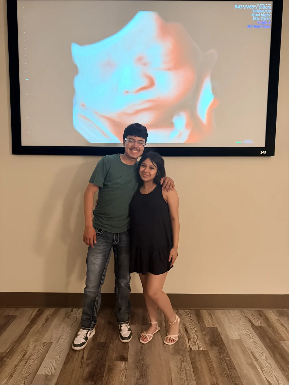 Two studio guests smiling beneath a large projected 4D ultrasound at 4D Sneak Peek