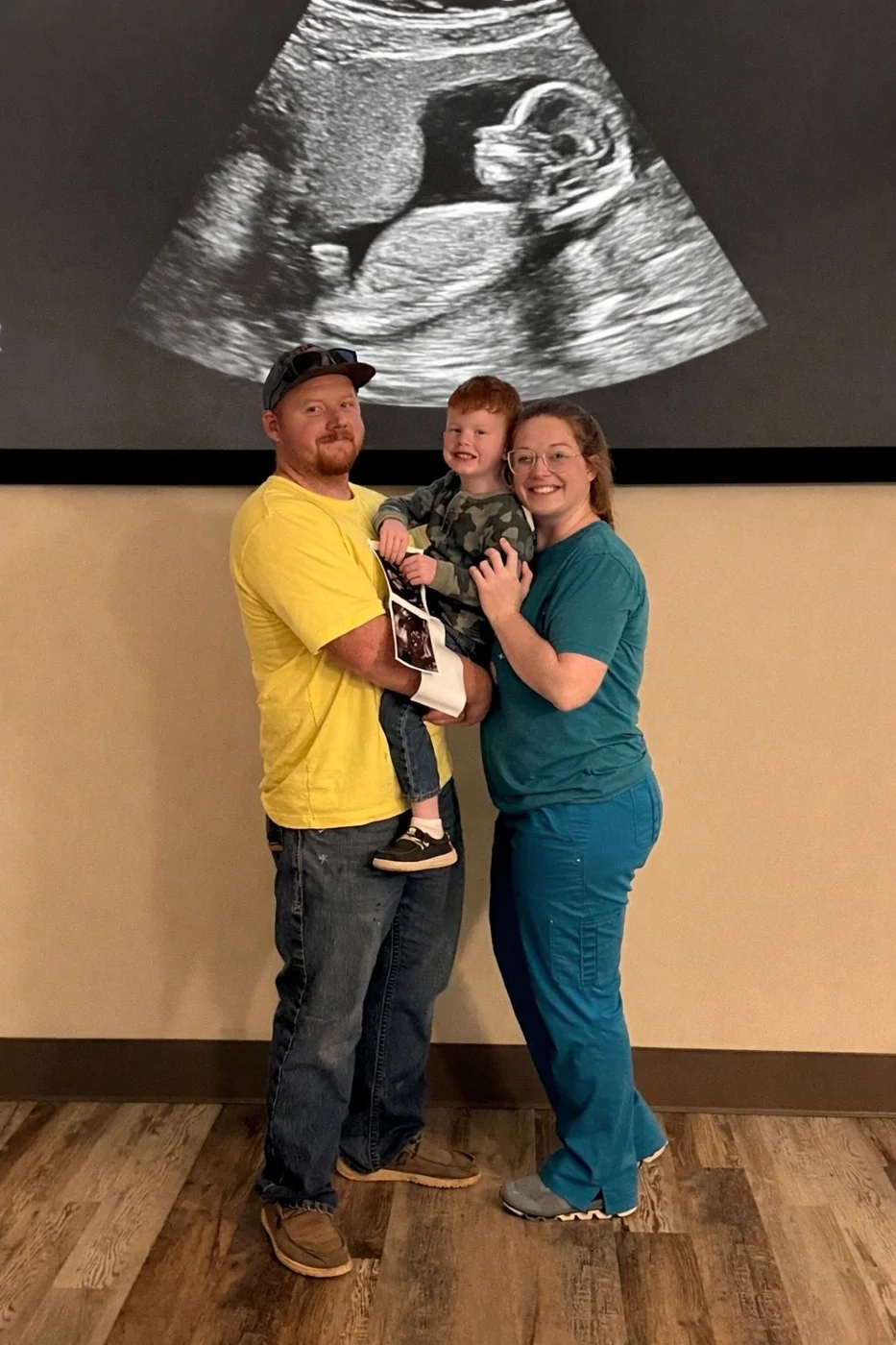 Two adults holding a child beneath a large projected ultrasound image in the studio